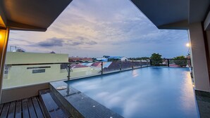 Una piscina en la azotea con vistas despejadas de los edificios circundantes y un cielo al atardecer.