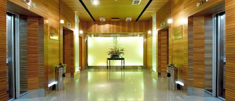 A modern hotel lobby with wooden paneling, a central floral arrangement, and a polished floor.