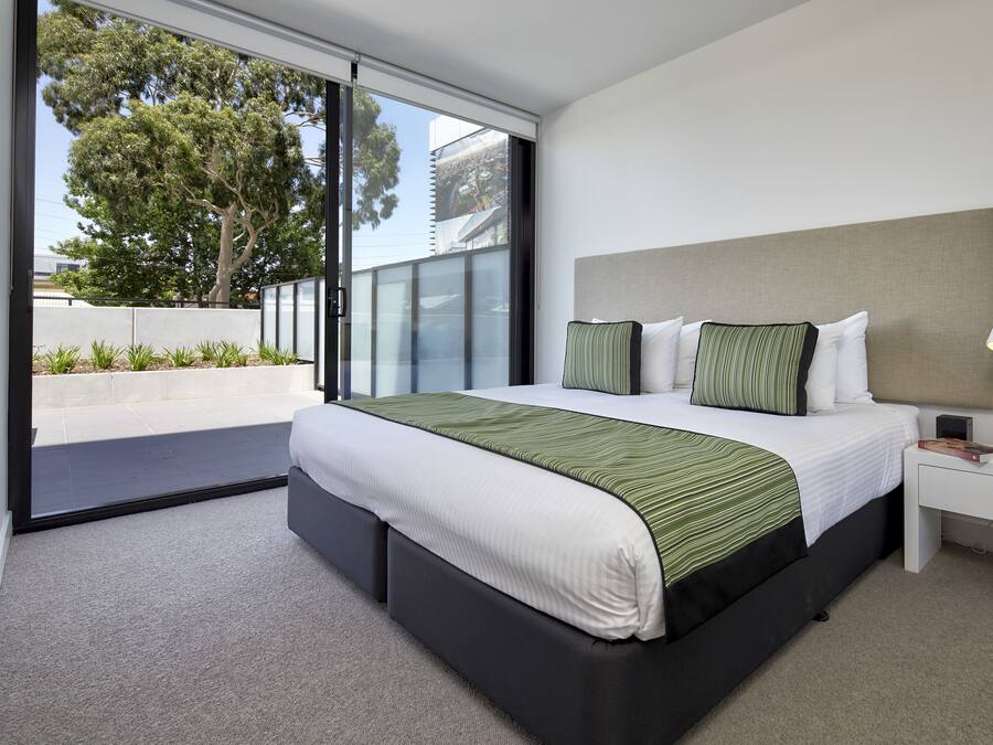 Een moderne slaapkamer met een groot bed, een nachtkastje en uitzicht op een balkon.