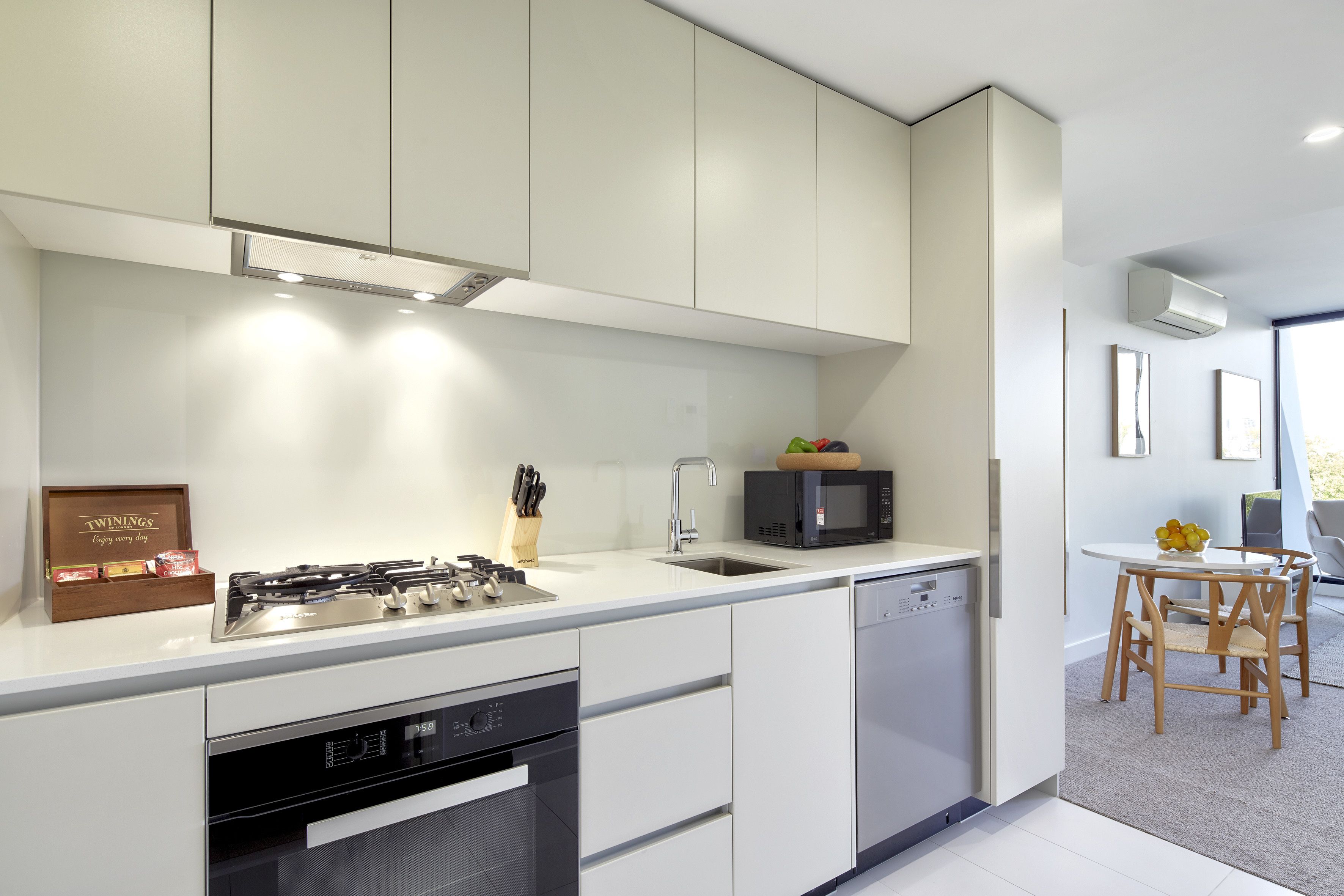 Una cucina moderna con mobili bianchi, piano cottura integrato e forno a microonde. Si nota un lavello e una lavastoviglie.