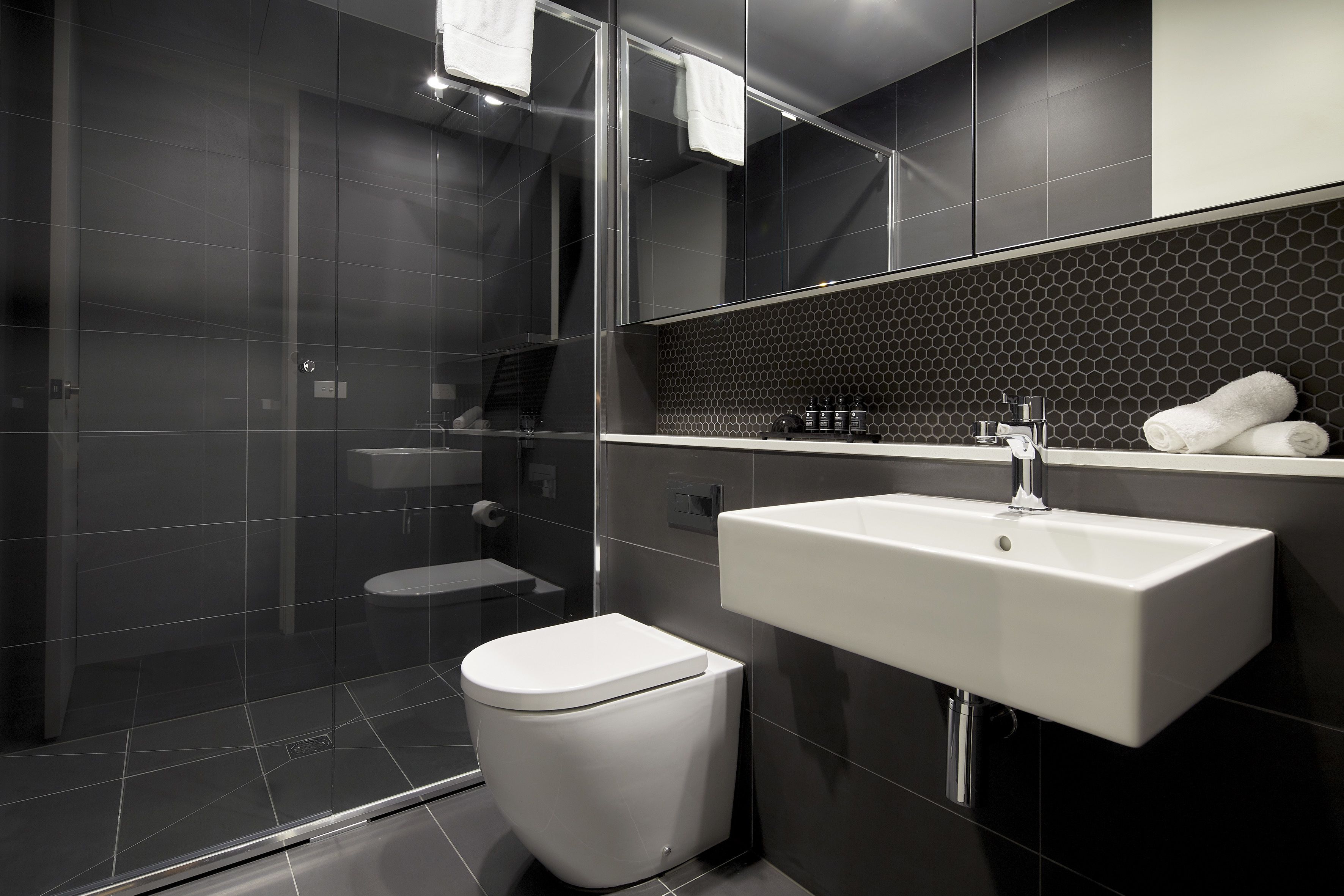 Un baño moderno con cabina de ducha de vidrio, inodoro blanco y lavamanos blanco con espejo arriba.