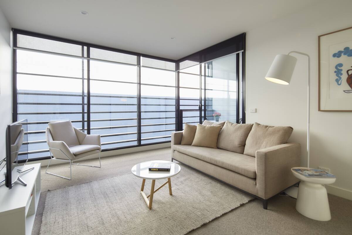 Una sala de estar moderna con sofá, sillón, mesa de centro, ventanas amplias con vistas y una lámpara de pie.