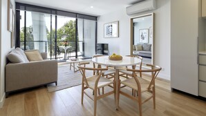 A modern living room with a sofa, dining table, and chairs, a balcony with a view, and an air conditioning unit on the wall. - 381 Cremorne (Cremorne)