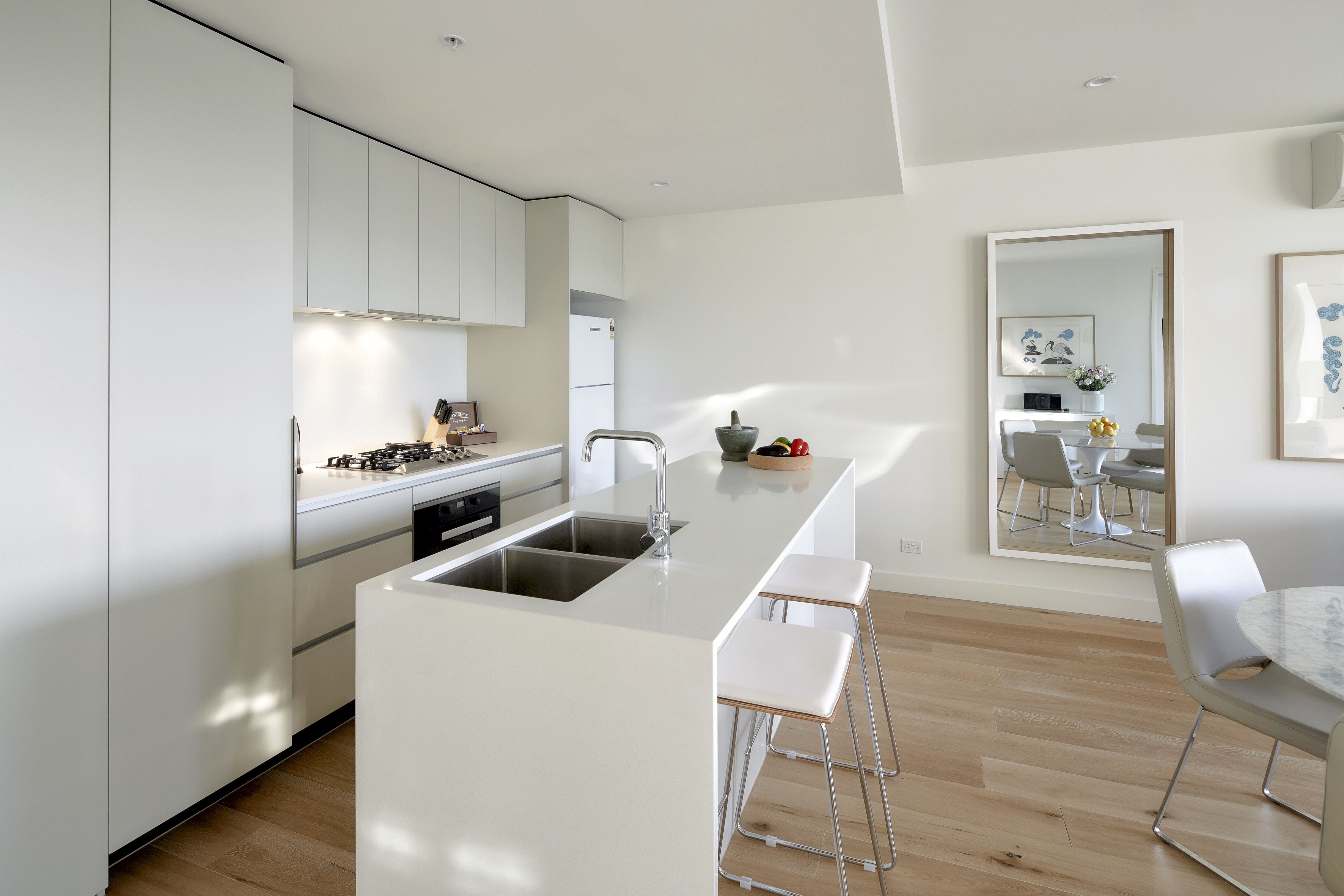 A modern kitchen with white cabinetry, a central island with stools, a dining area with a table and chairs, and a large mirror on the wall.