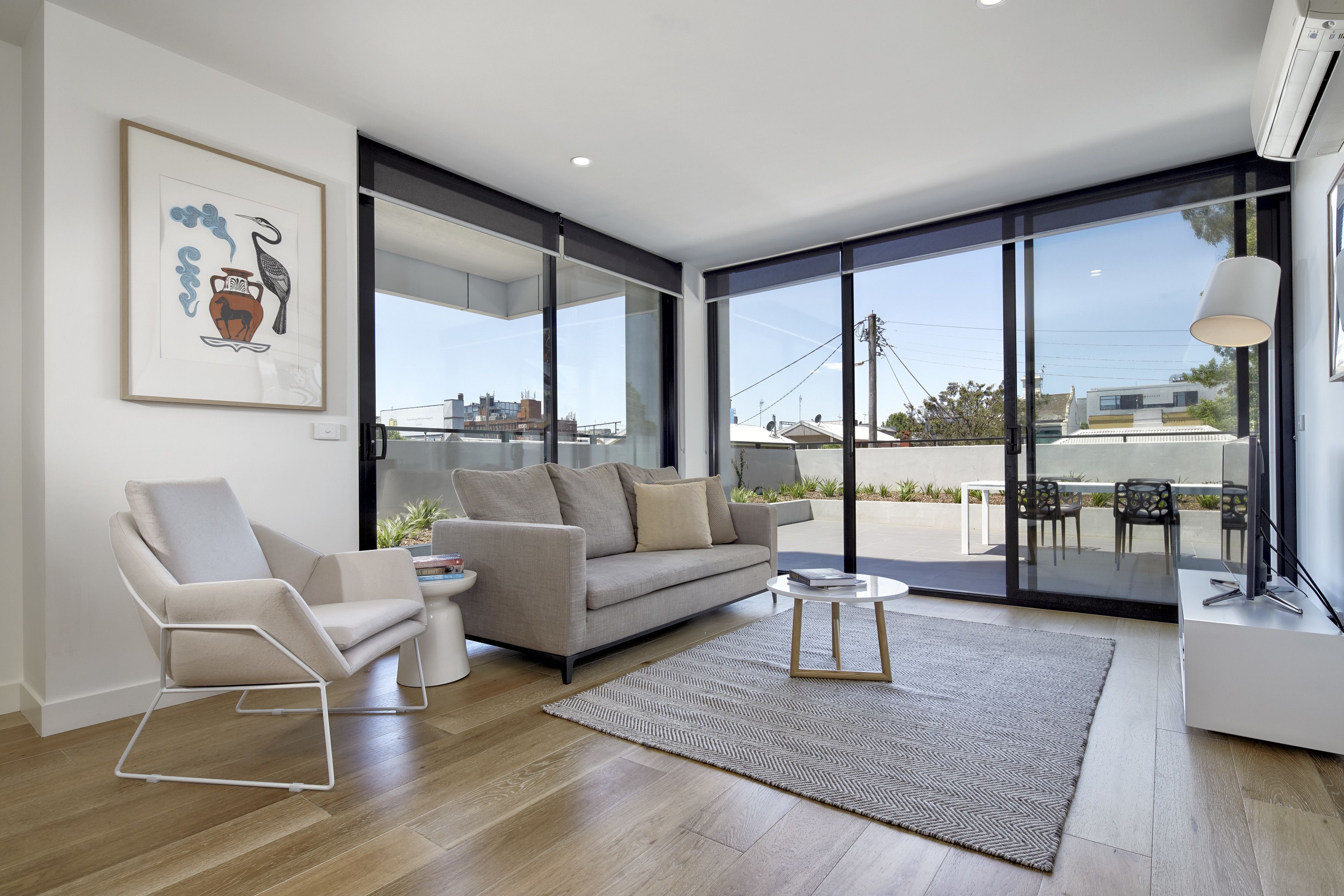 A modern living room with a sofa, armchair, and coffee table, large windows, and a city view.