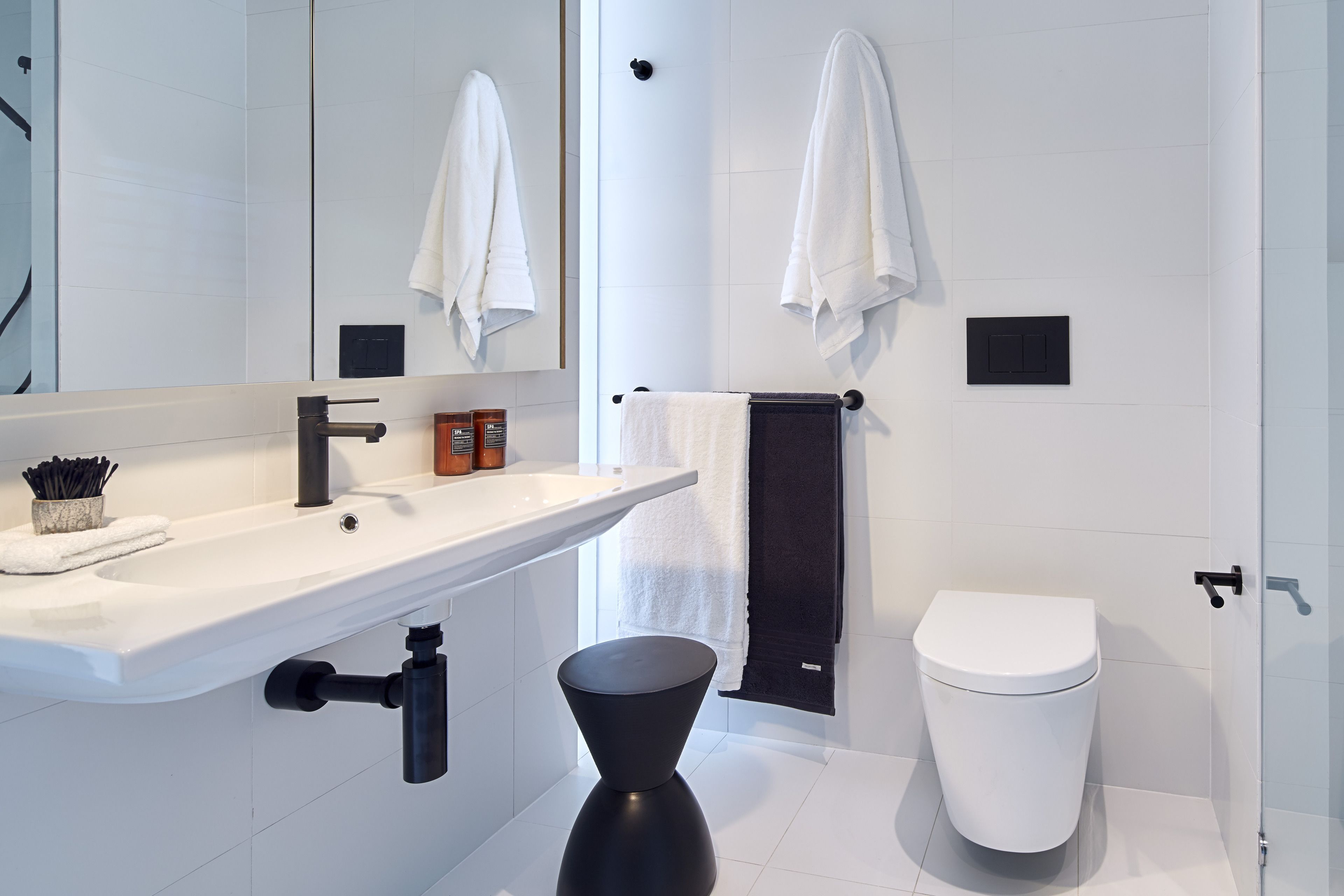 A modern bathroom with a white sink, black faucet, and a black toilet.