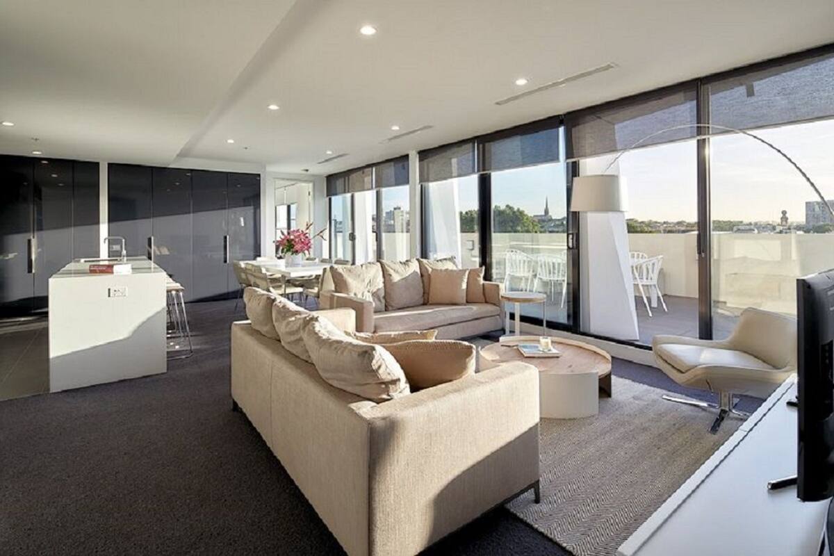 Una sala de estar moderna con sofá, mesa de centro y televisor. Hay un comedor con una mesa y sillas. La habitación tiene ventanas amplias y un balcón con vistas.