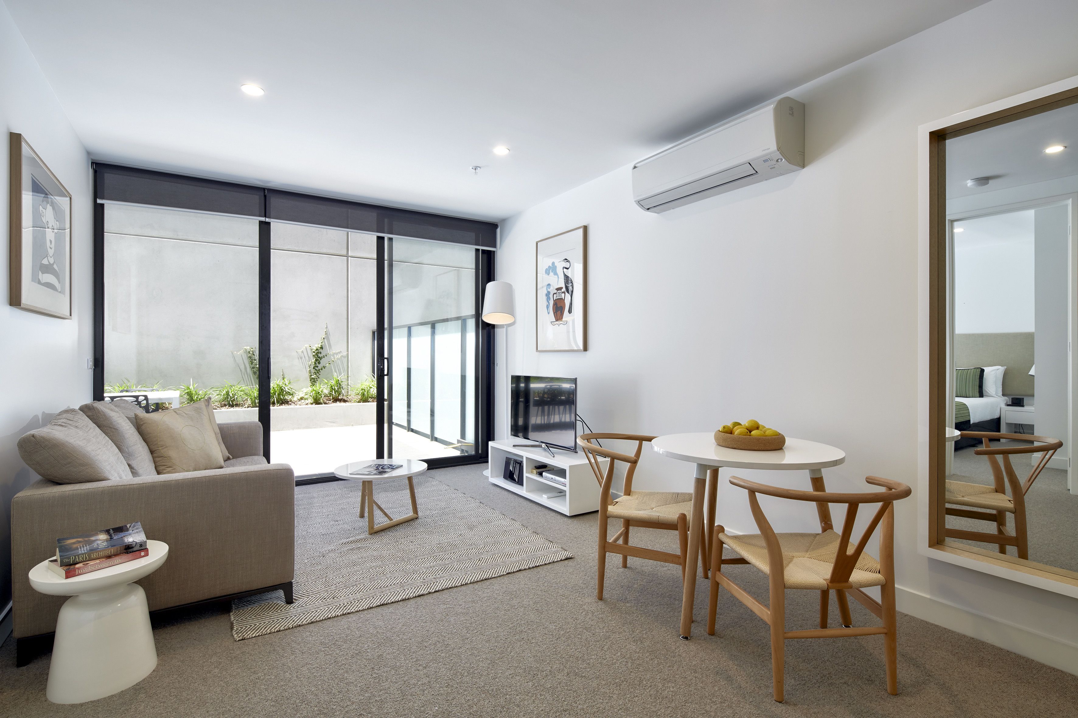 A modern living room with a sofa, a TV, a dining table with chairs, and a large window.