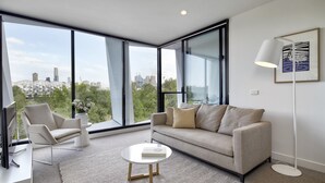 A modern living room with a sofa, armchair, and coffee table, large windows offering a city view, and a floor lamp. - 381 Cremorne (Cremorne)