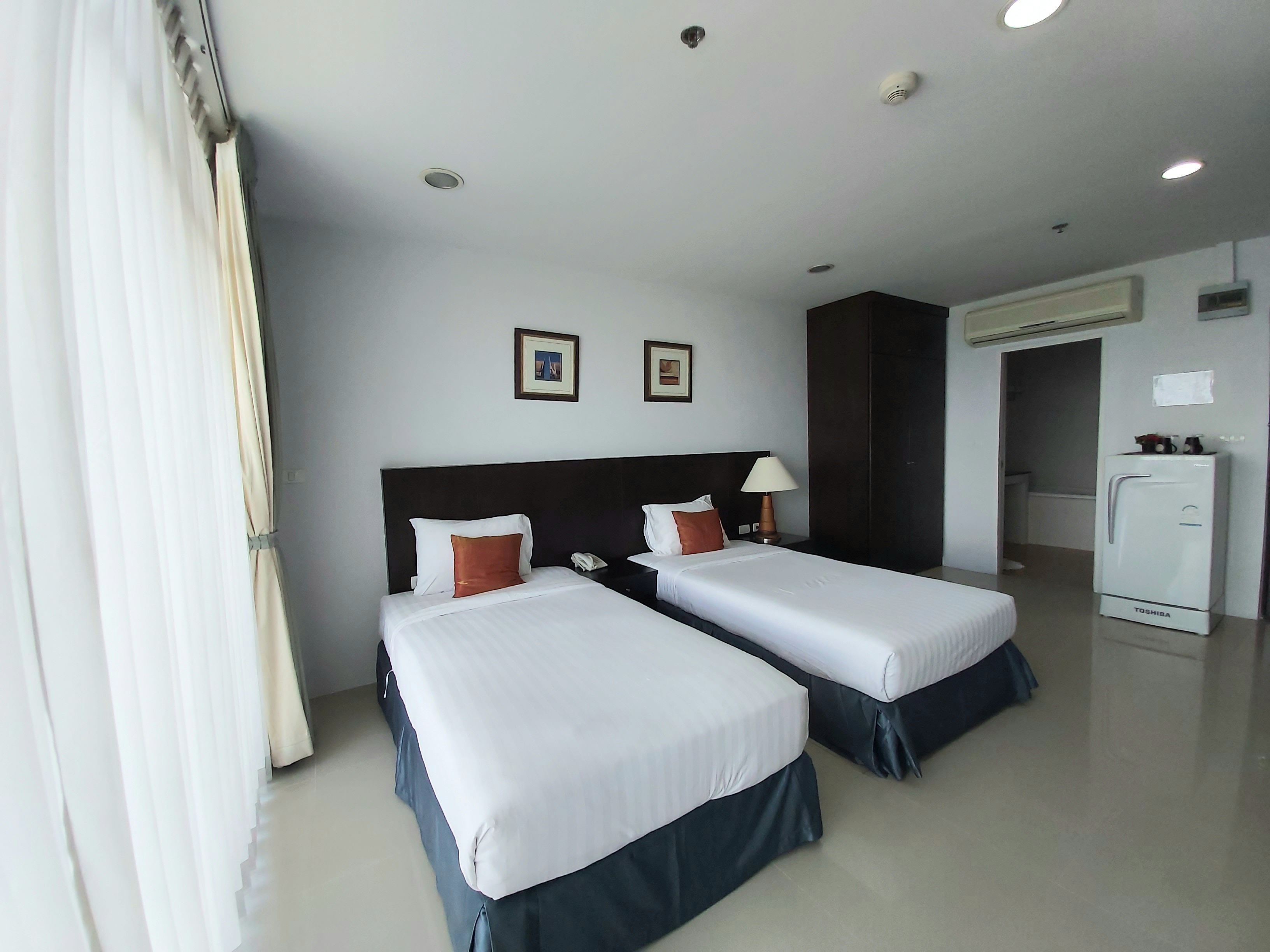 A hotel room with two beds, a refrigerator, a desk, and a bathroom visible through an open door.