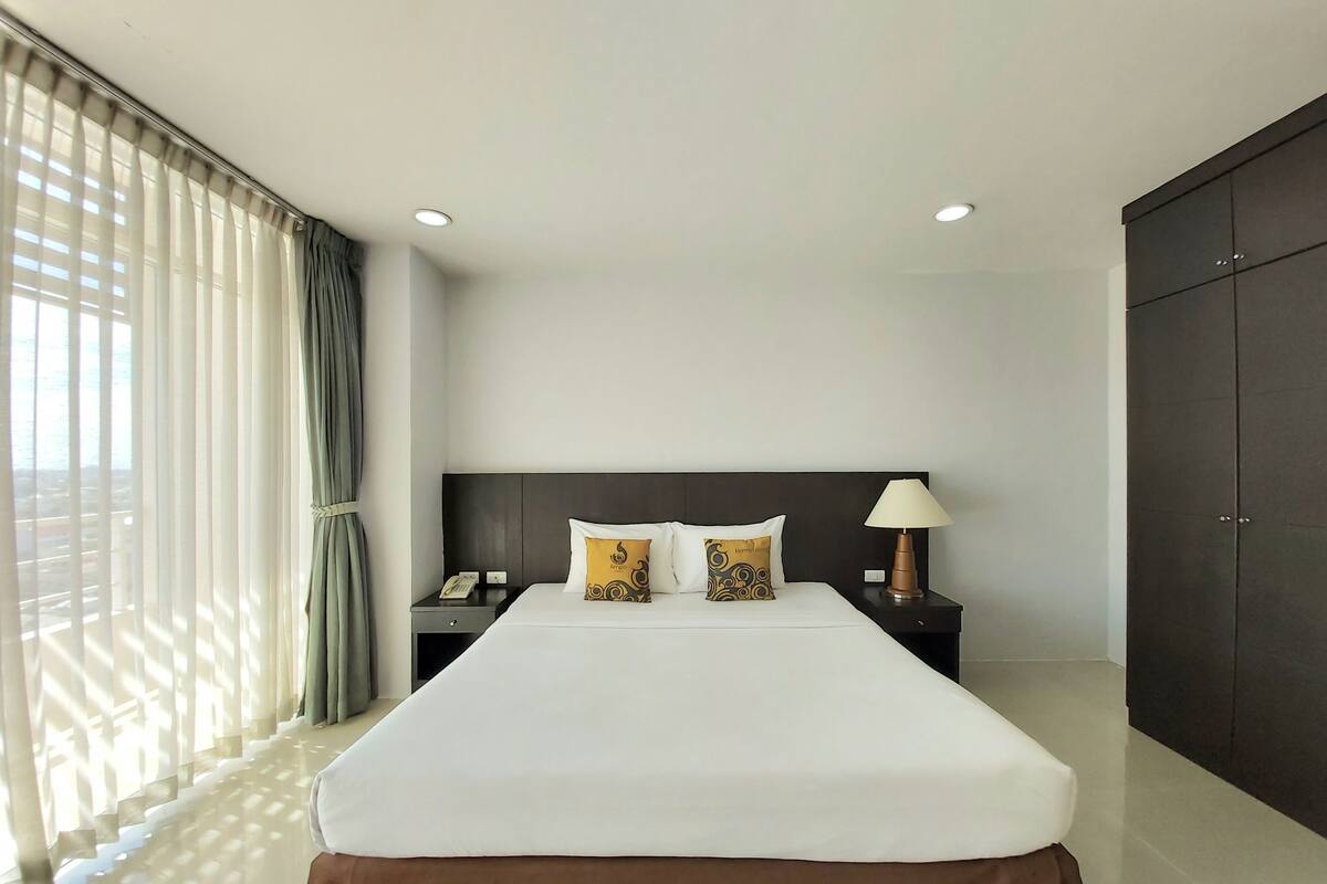 Habitación de hotel con una cama grande, una mesita de noche con lámpara, teléfono y armario.