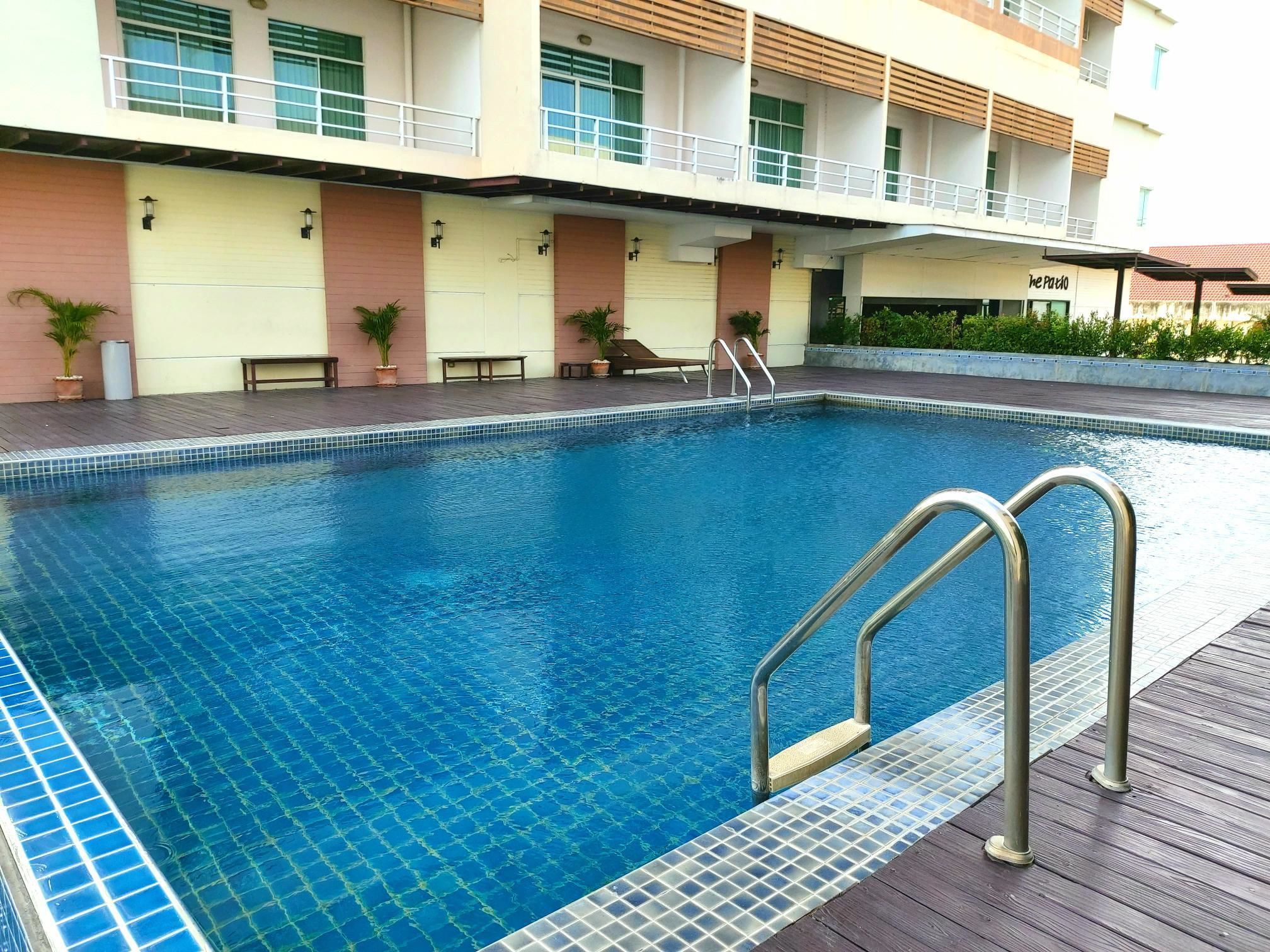 A swimming pool with a tiled edge, metal handrails, and potted plants around the pool area.