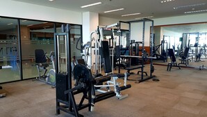 Ein Fitnessstudio mit unterschiedlichen Trainingsgeräten, großen Spiegeln und einem Teppichboden.