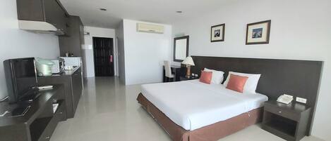 Una habitación de hotel con cama, mesitas de noche, un escritorio con computadora y una kitchenette.