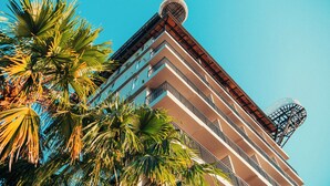 A multi-story hotel with balconies, a rooftop helipad, and palm trees in the foreground. - The Elephant Crossing Hotel (Vang Vieng)