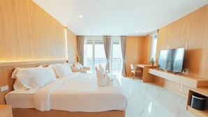 A modern hotel room with a large bed, a desk, a television, and a balcony with curtains. - The Elephant Crossing Hotel (Vang Vieng)