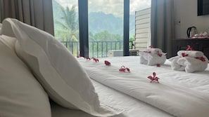 Ein Hotelzimmer mit Bett, Kissen, Handtüchern und Blick auf Berge und Palmen.