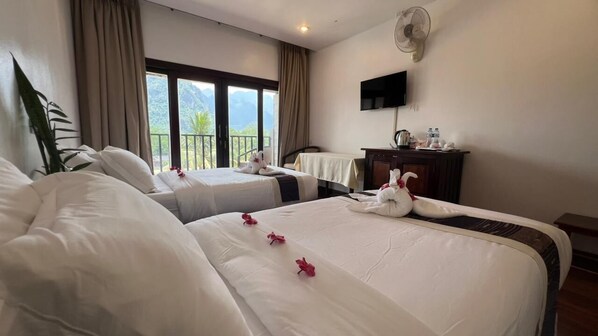 A hotel room with two beds, a TV, a desk, and a balcony with a mountain view.