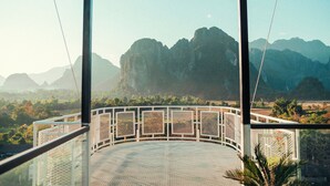 A view from a balcony with a metal railing, overlooking a mountainous landscape. - The Elephant Crossing Hotel (Vang Vieng)