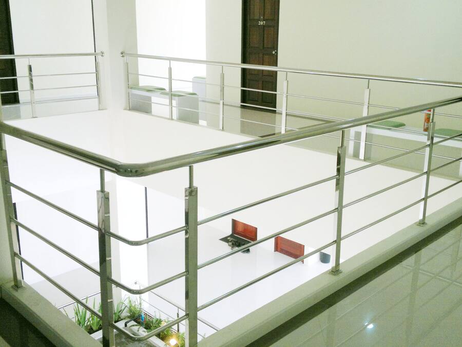 A spacious, modern indoor area with a metal railing, a flat white floor, and a door marked with the number 207.