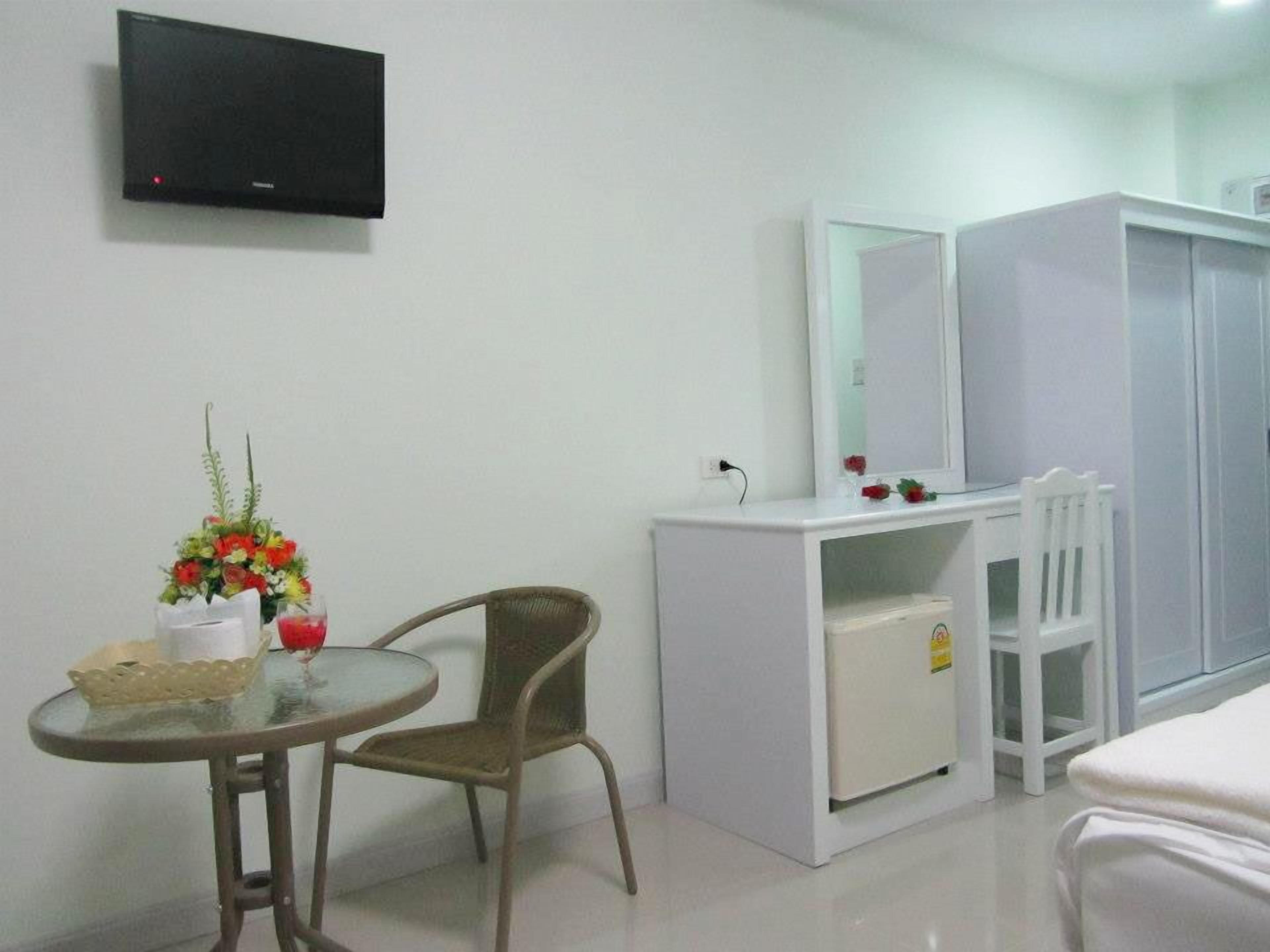 A hotel room with a bed, a desk with a chair, a TV mounted on the wall, and a wardrobe.