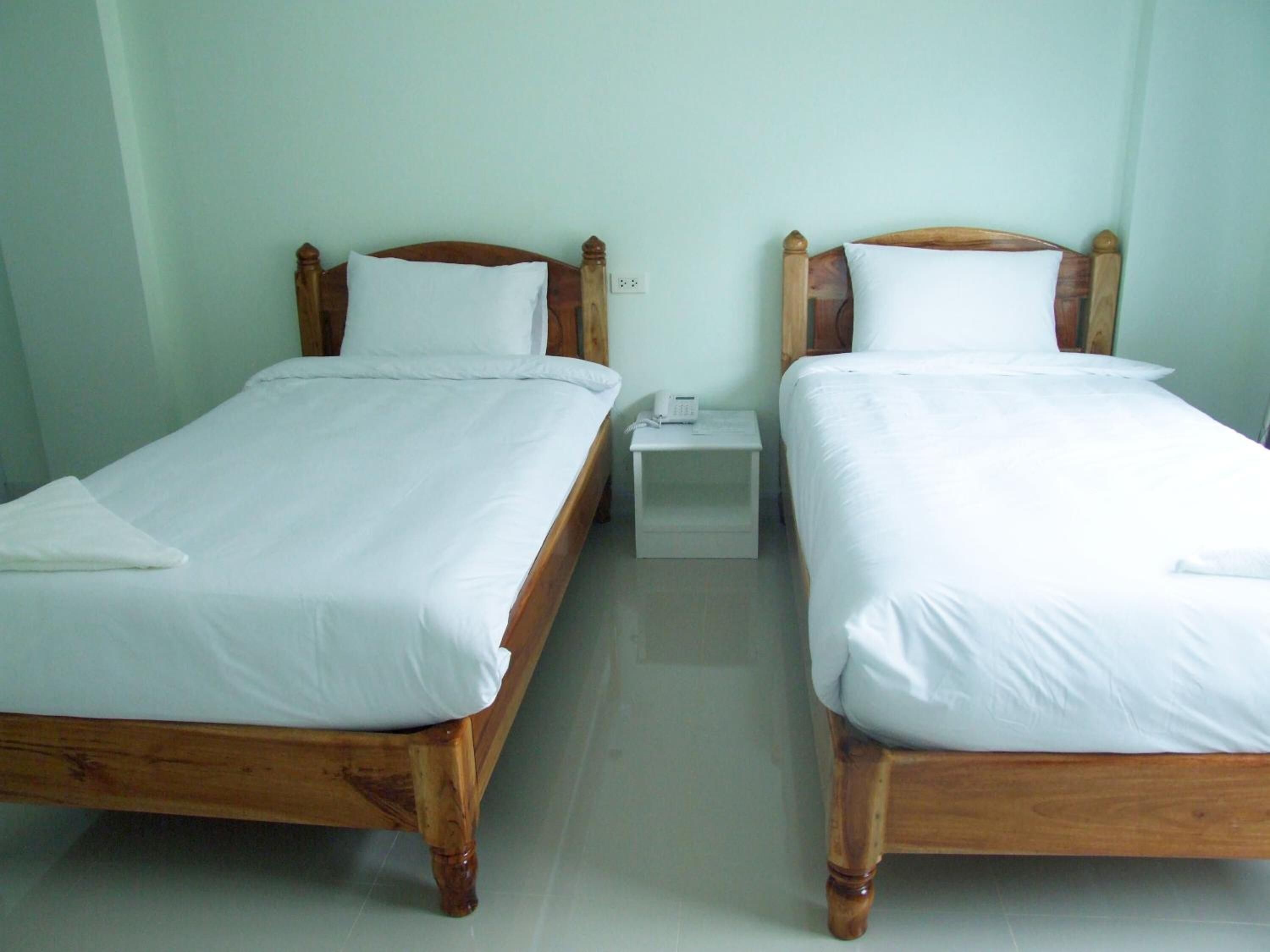 Duas camas de solteiro com estruturas de madeira e roupa de cama branca, uma pequena mesa de cabeceira com telefone, e uma parede verde-clara.