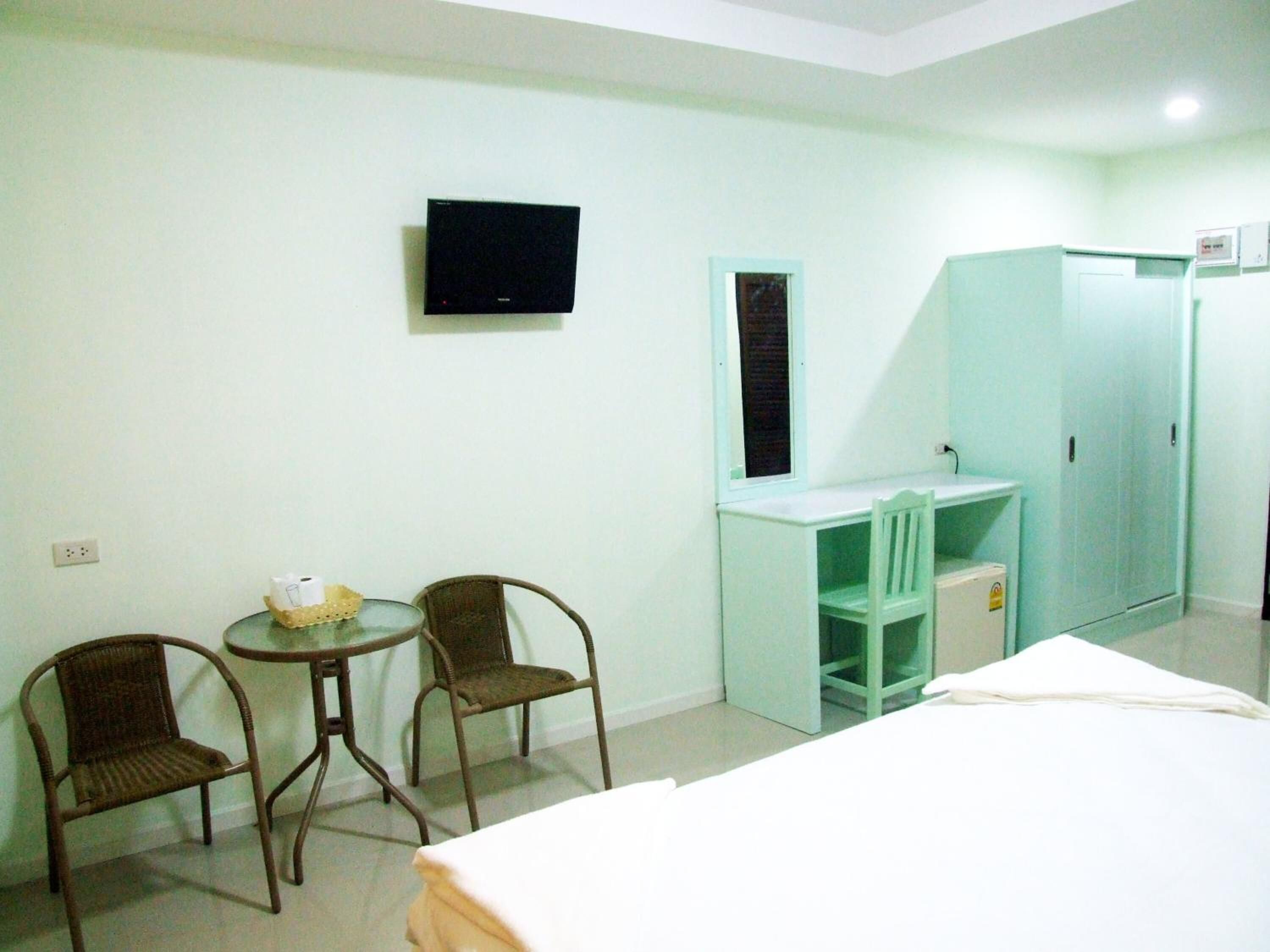 A hotel room with a bed, two chairs, a small table with a basket, a desk with a chair, a TV mounted on the wall, and a wardrobe.