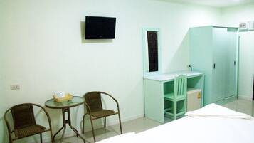 A hotel room with a bed, two chairs, a small table with a basket, a desk with a chair, a TV mounted on the wall, and a wardrobe.