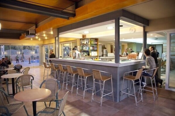 Una zona de bar con barra, taburetes y mesas.