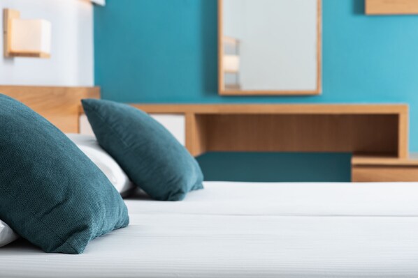 Una cama con almohadones color turquesa y un cabecero de madera en una habitación con paredes color turquesa y un espejo sobre la cama.