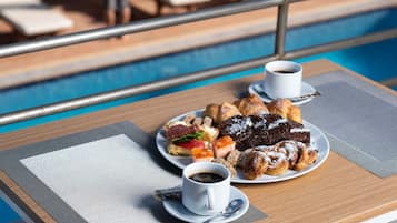 A table with a plate of pastries and two cups of coffee, overlooking a pool area.