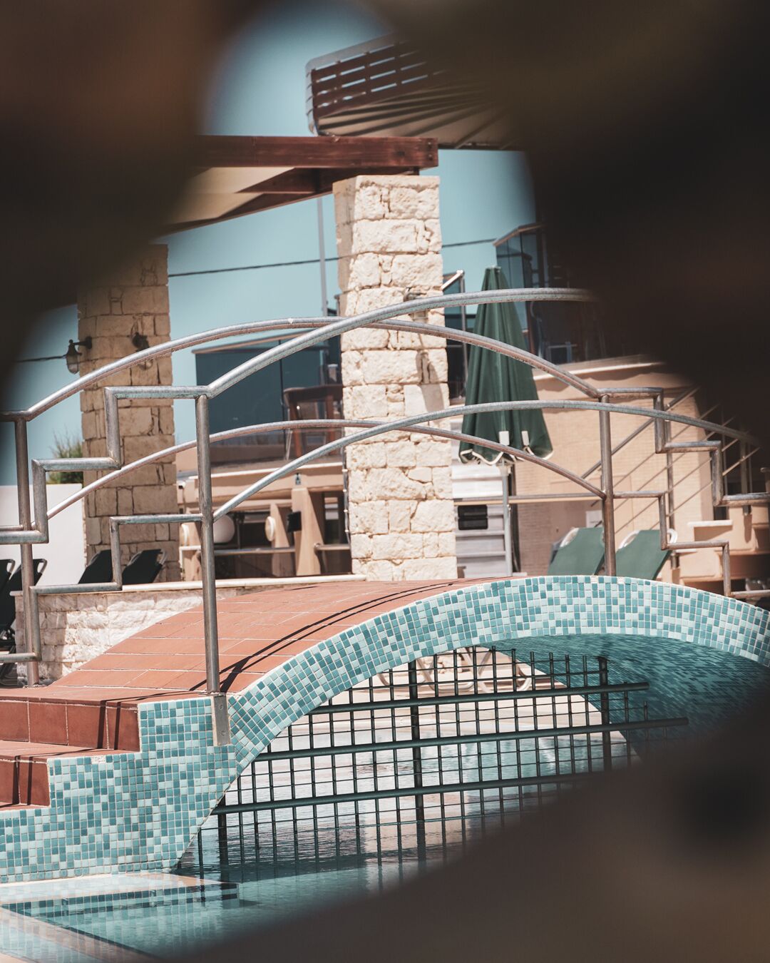 A pool area with a tiled border, a stone pillar, and a metal railing.