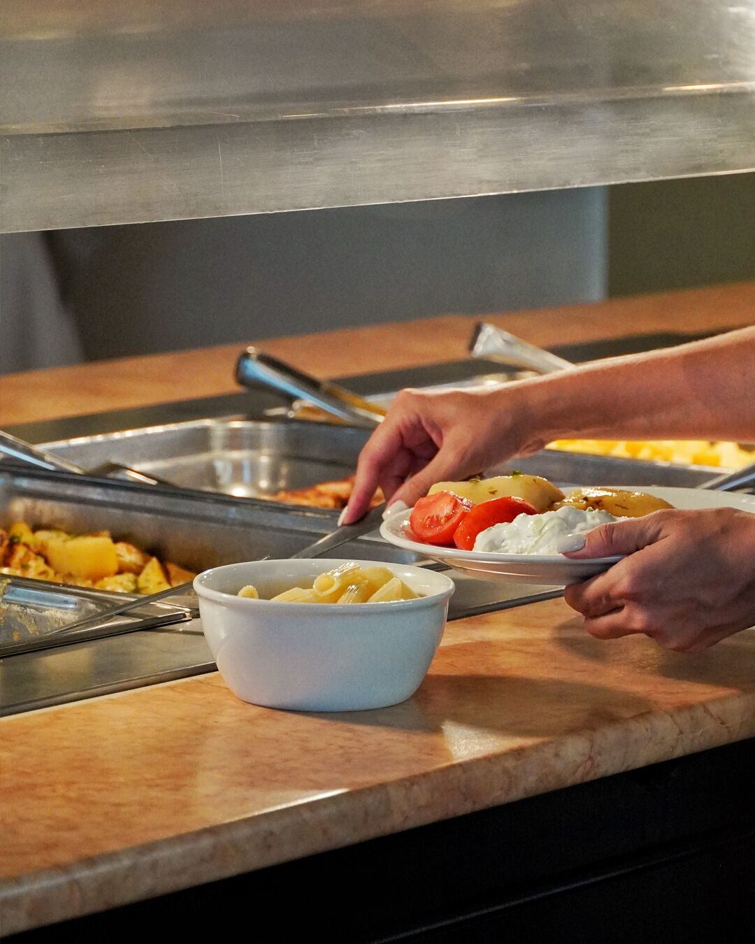 Buffet com diversos pratos, incluindo um recipiente com massa e um prato com tomates e cobertura cremosa.