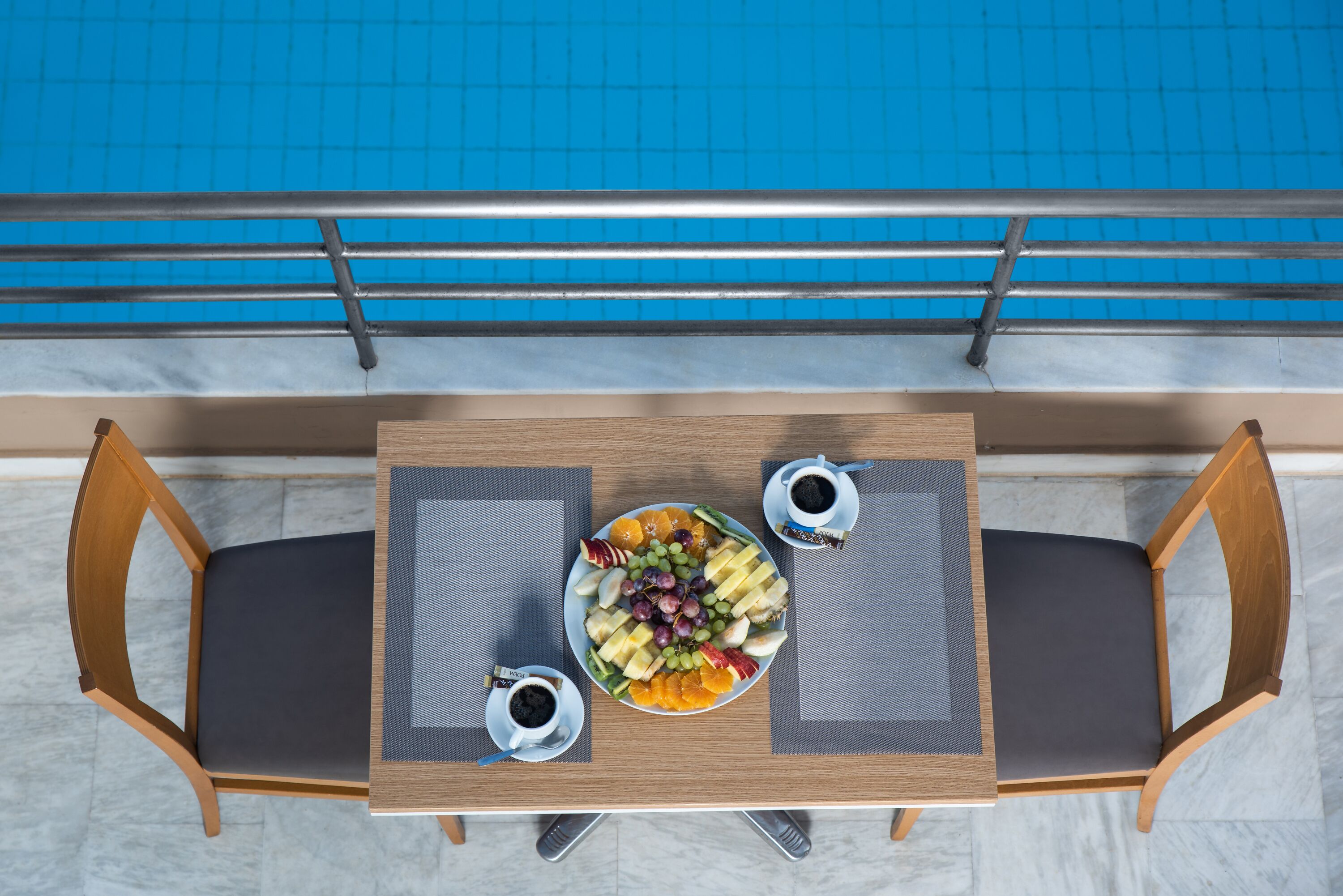 A dining table with a fruit platter, two cups of coffee, and two wooden chairs.