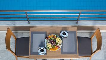 A dining table with a fruit platter, two cups of coffee, and two wooden chairs.