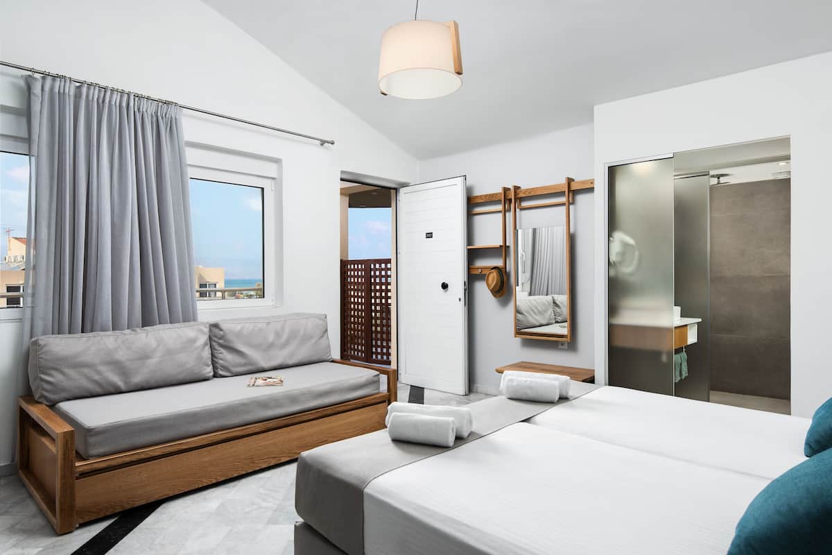 Ett modernt hotellrum med en soffa, en säng, ett badrum med spegel och utsikt över staden.