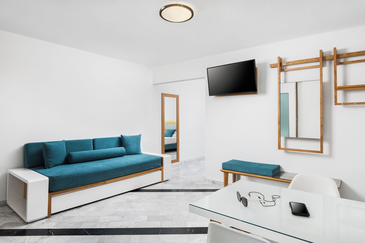 A modern room with a teal sofa, a white desk, and a flat-screen TV mounted on the wall.
