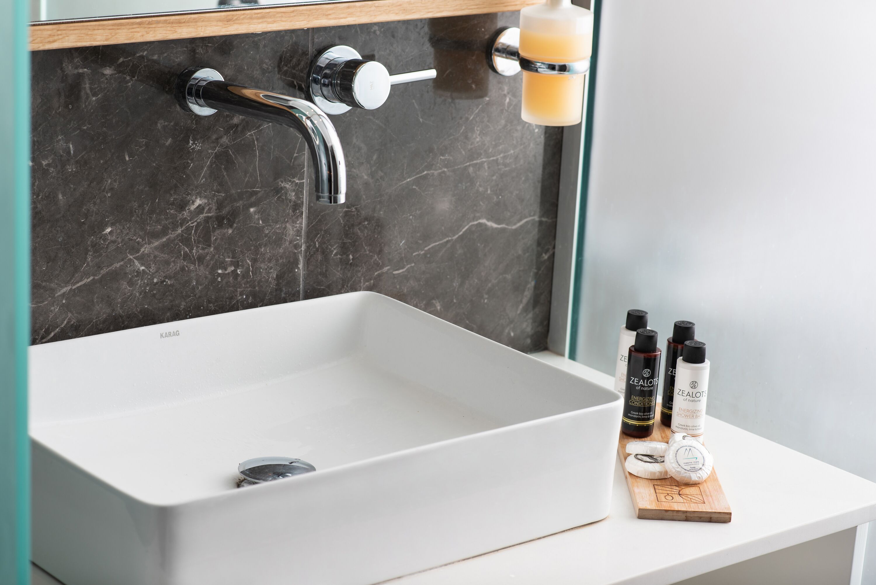 Un baño con un lavabo blanco, pared de mármol y un estante con artículos de aseo.