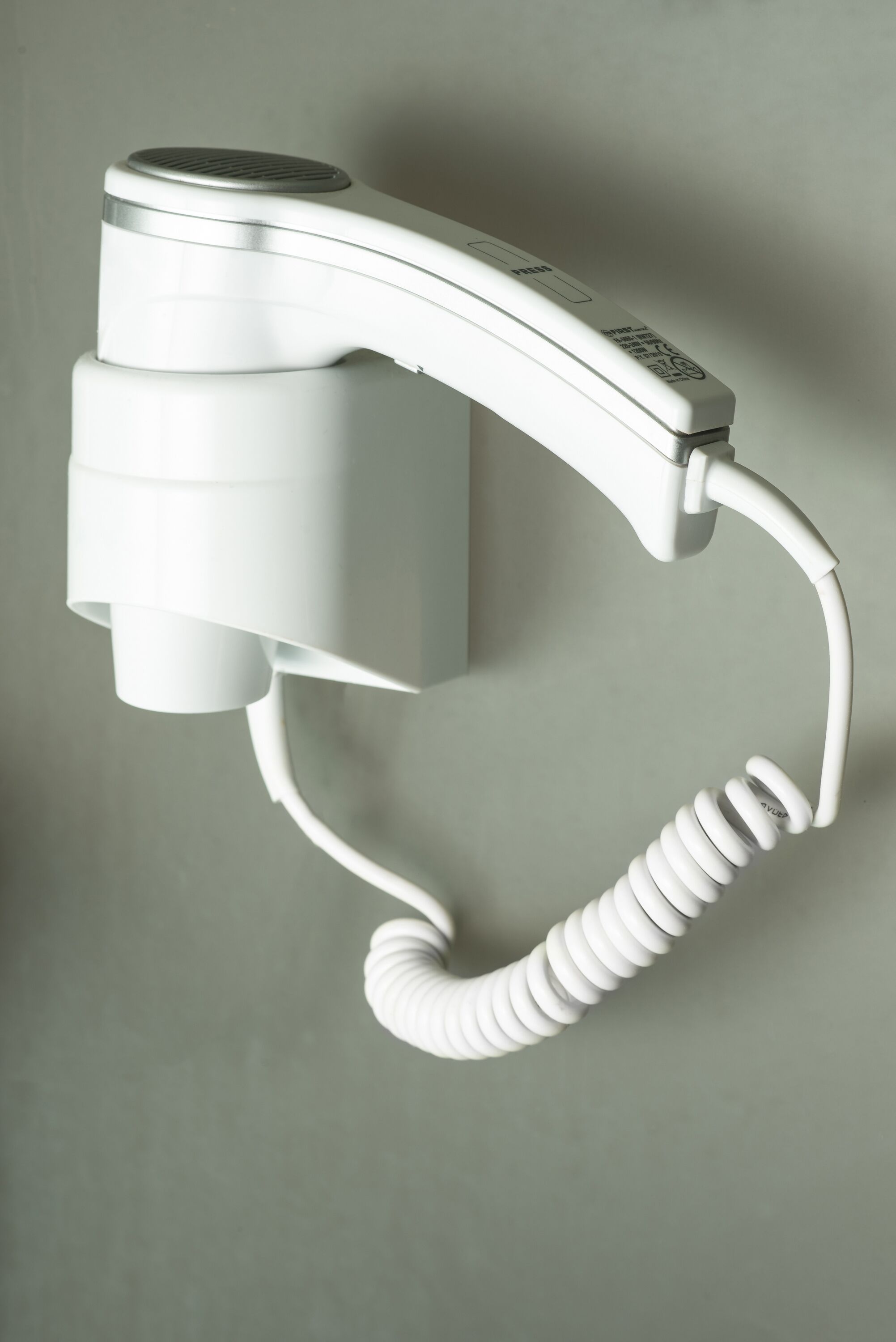 Een witte haardroger bevestigd aan een muur met een opgerolde snoer.