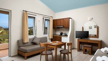 A compact living space with a sofa, dining table, chairs, a small kitchen area, a television, and a balcony with curtains.