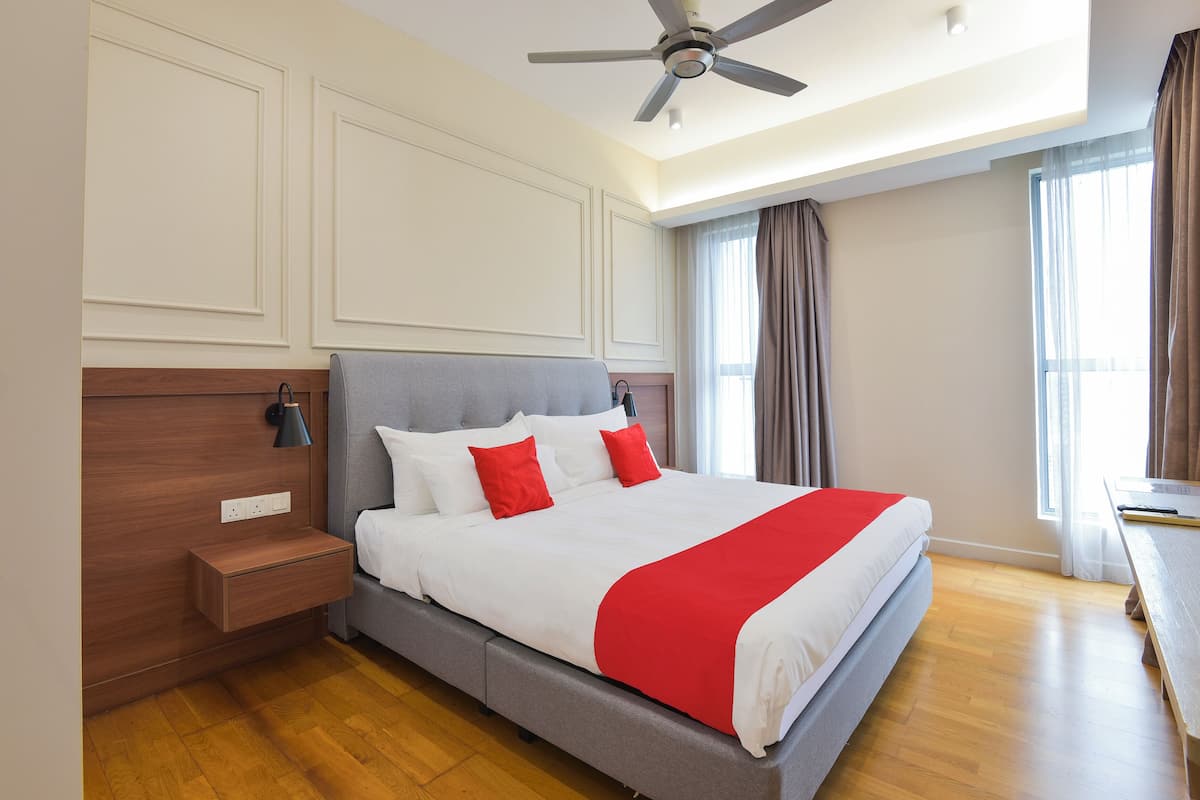 Habitació d'hotel amb un llit gran, un ventilador de sostre, una taula de nit i una finestra amb cortines.
