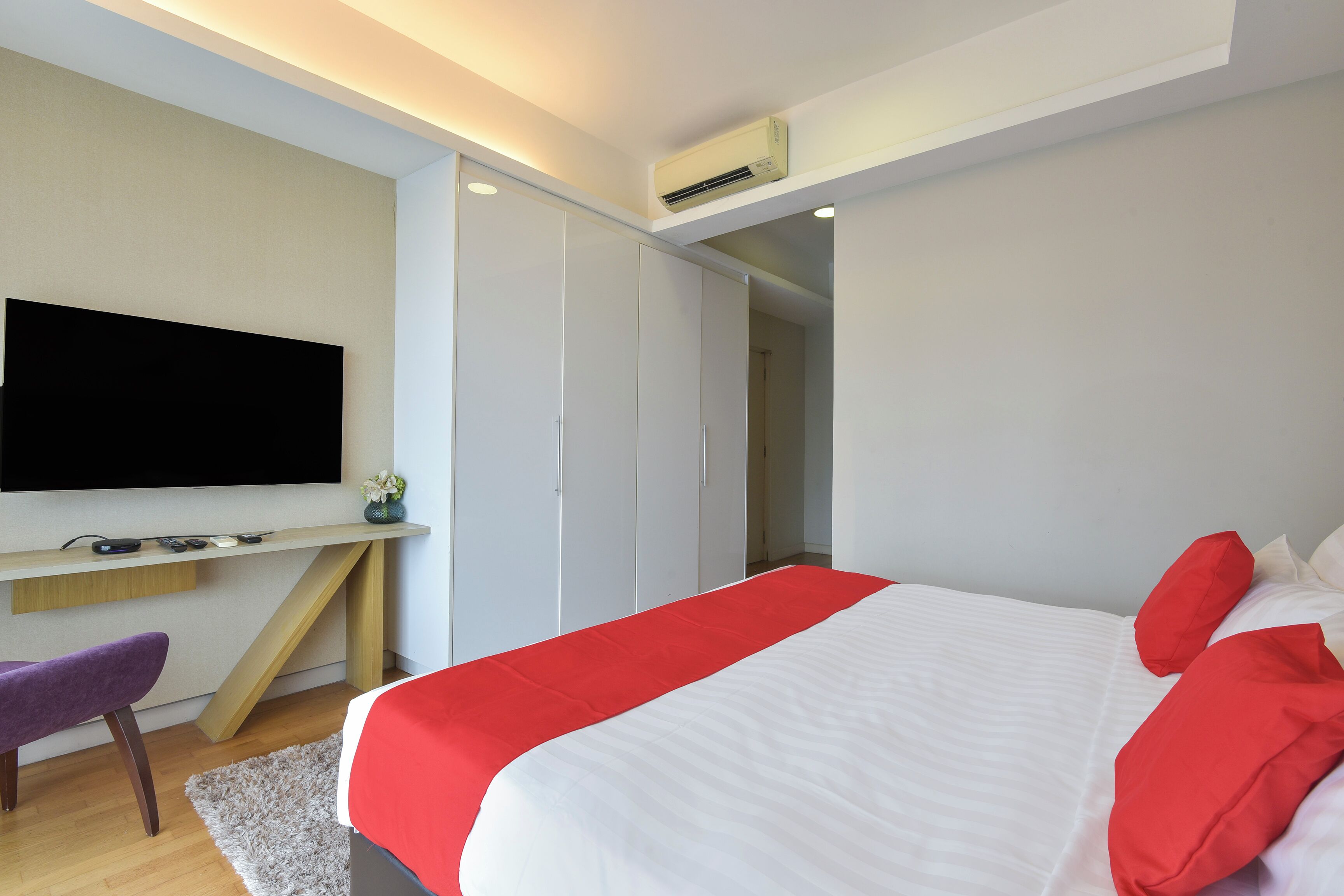 A modern bedroom with a bed, a desk, and a TV.