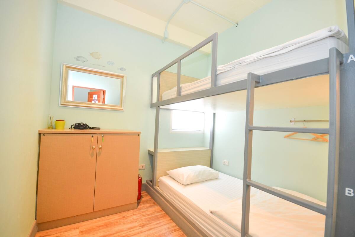 Une chambre avec un lit superposé, une armoire en bois et un miroir au mur.