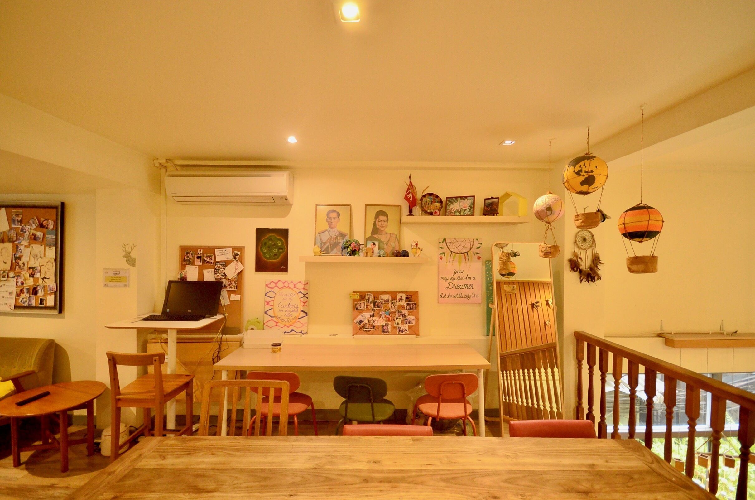 A cozy room with a wooden dining table, chairs, a laptop on a desk, and various wall decorations including framed pictures and a shelf with items.