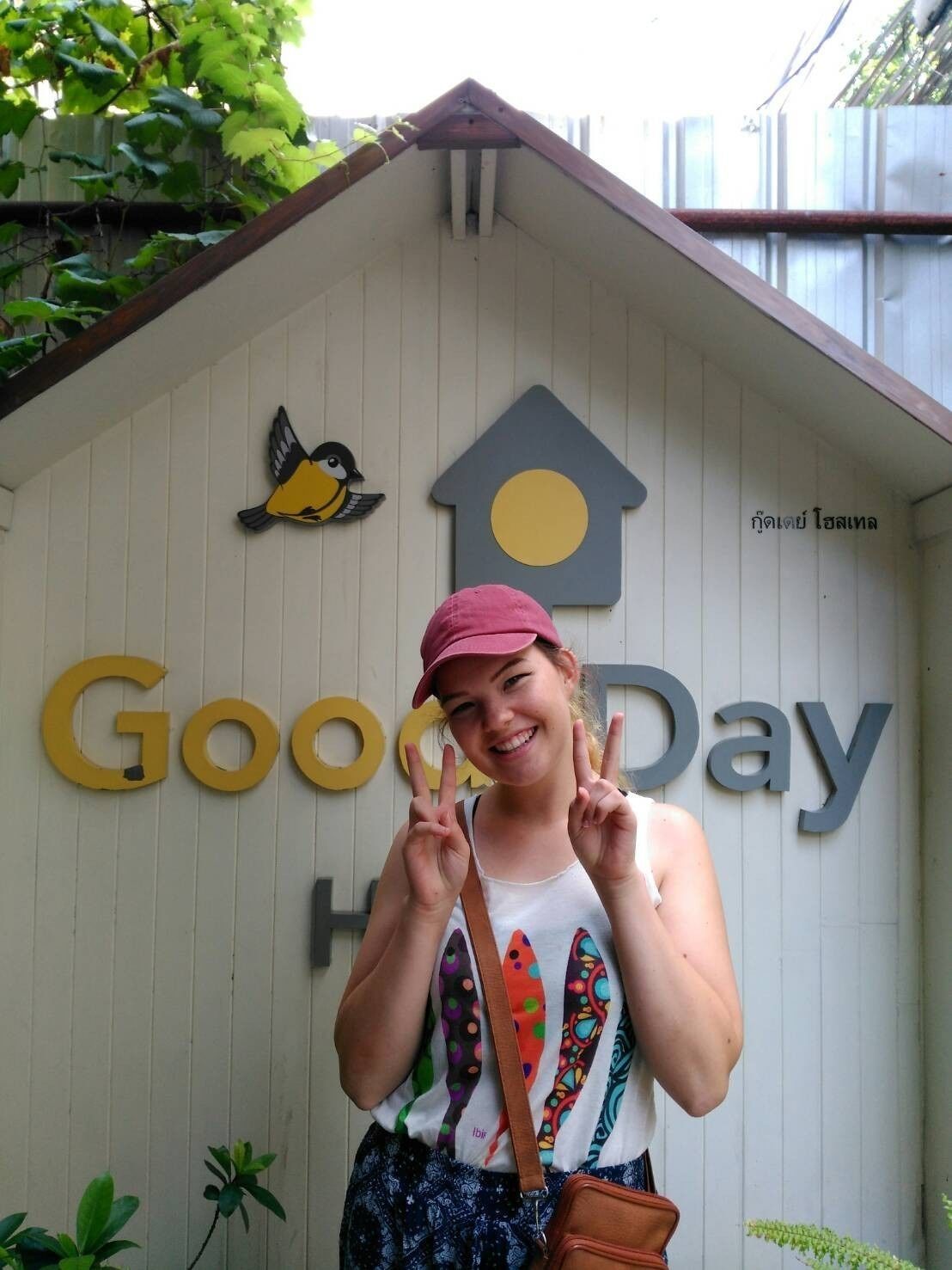 Una persona de pie frente a un edificio con un cartel que dice 'Good Day', un comedero para pájaros y una decoración con forma de casa.