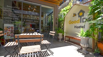 An outdoor seating area with wooden tables and chairs, a potted plant, and a sign for a hostel.