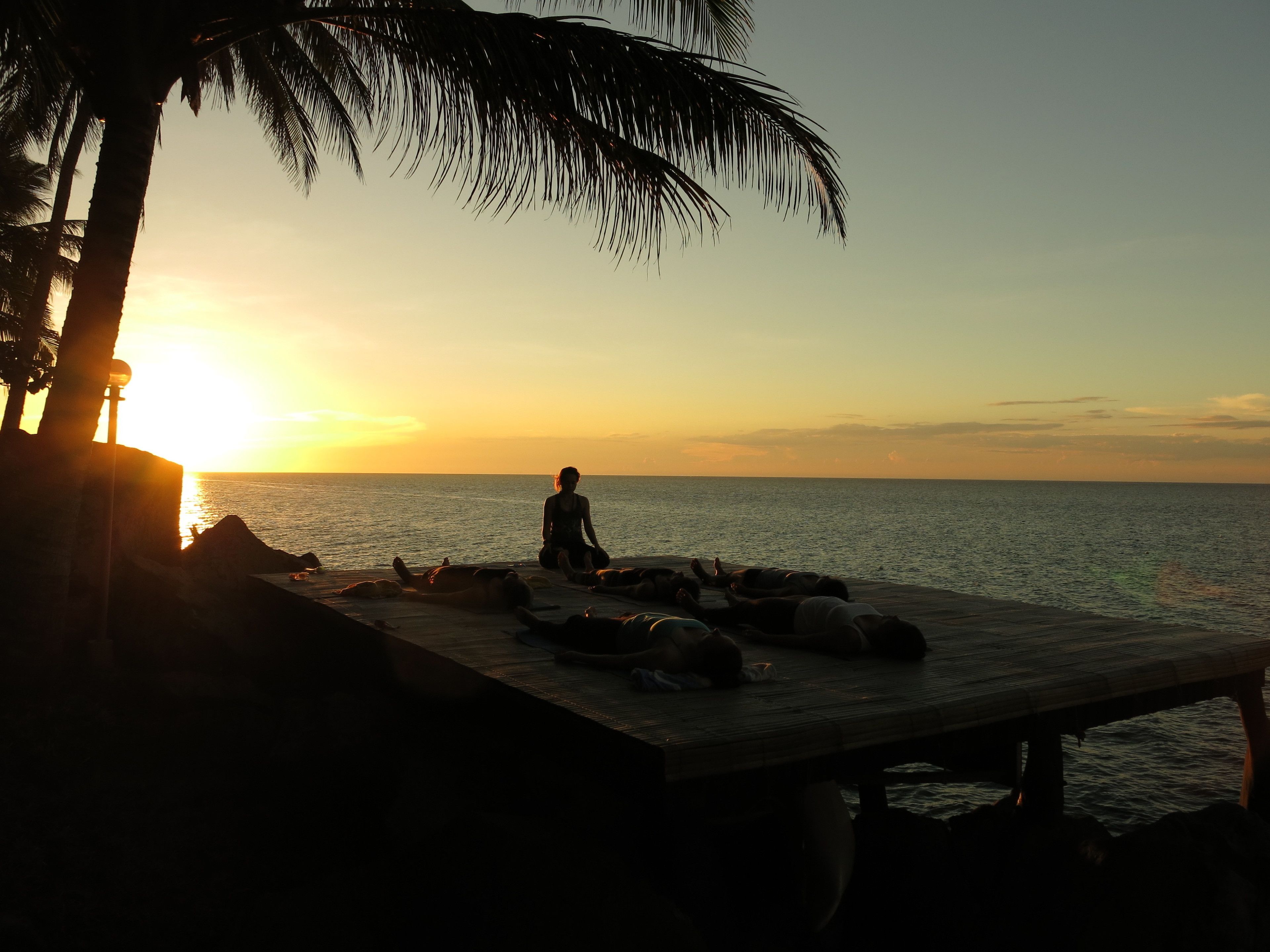 Escena de playa con una persona sentada en una plataforma de madera que domina el mar al atardecer.