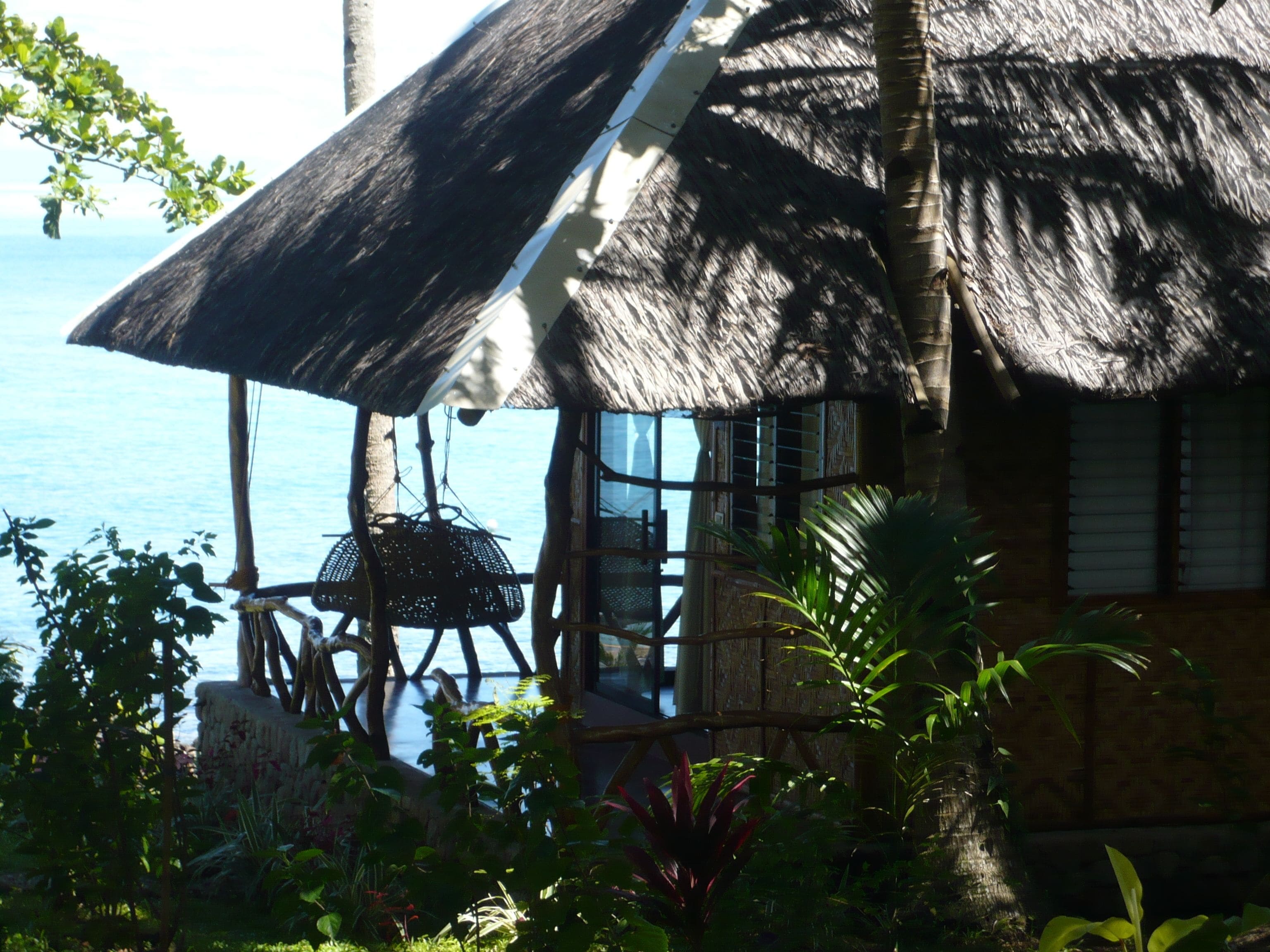 A thatched-roof structure with a view of the sea, surrounded by lush greenery.