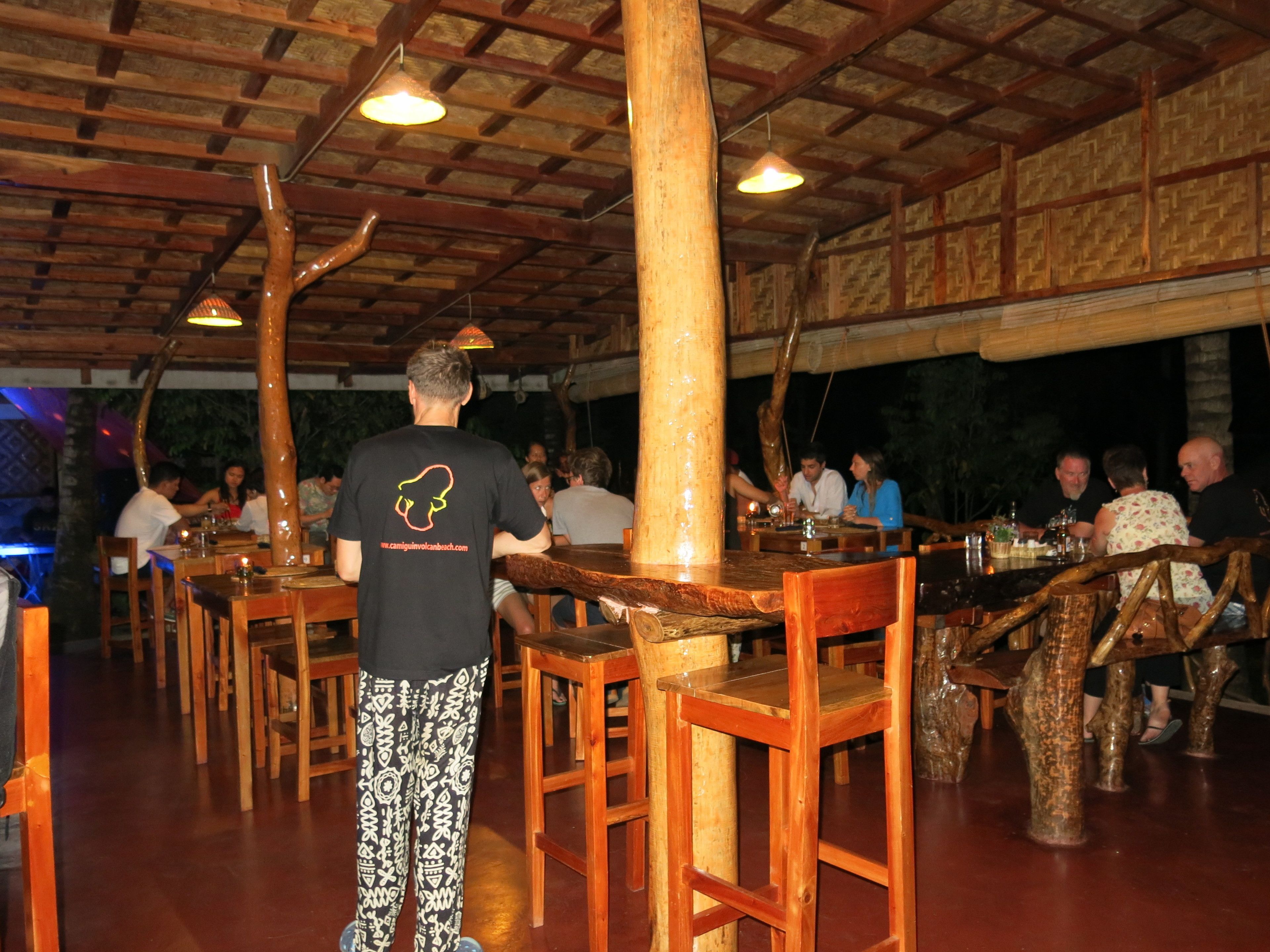 A restaurant with wooden tables and chairs, a high ceiling with exposed beams, and a rustic interior design.