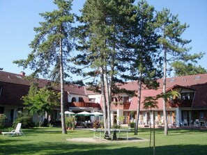 Traditional hotel with a central entrance and two wings, surrounded by a well-manicured lawn and garden.